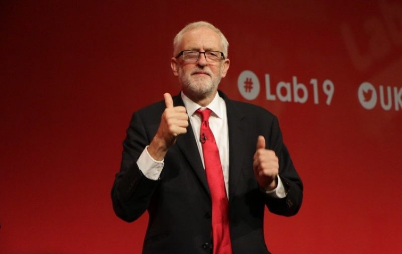 Jeremy Corbyn with two thumbs up in front of a #Lab19 sign
